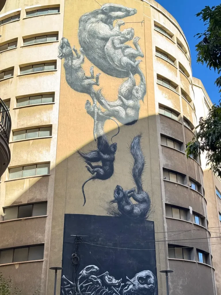 Gran mural de animales dibujados en blanco y negro cayendo sobre un fondo beige en un edificio de Málaga