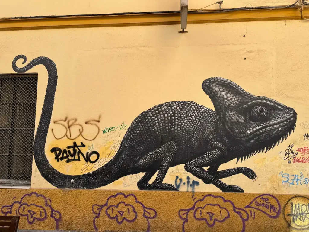 Mural realista de un camaleón negro pintado sobre una pared amarilla en el centro de Málaga